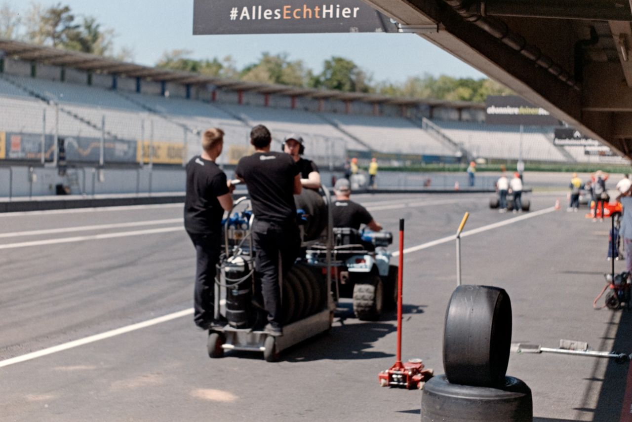 Pit crew preparing equipment on a motorsport track under bright daylight.