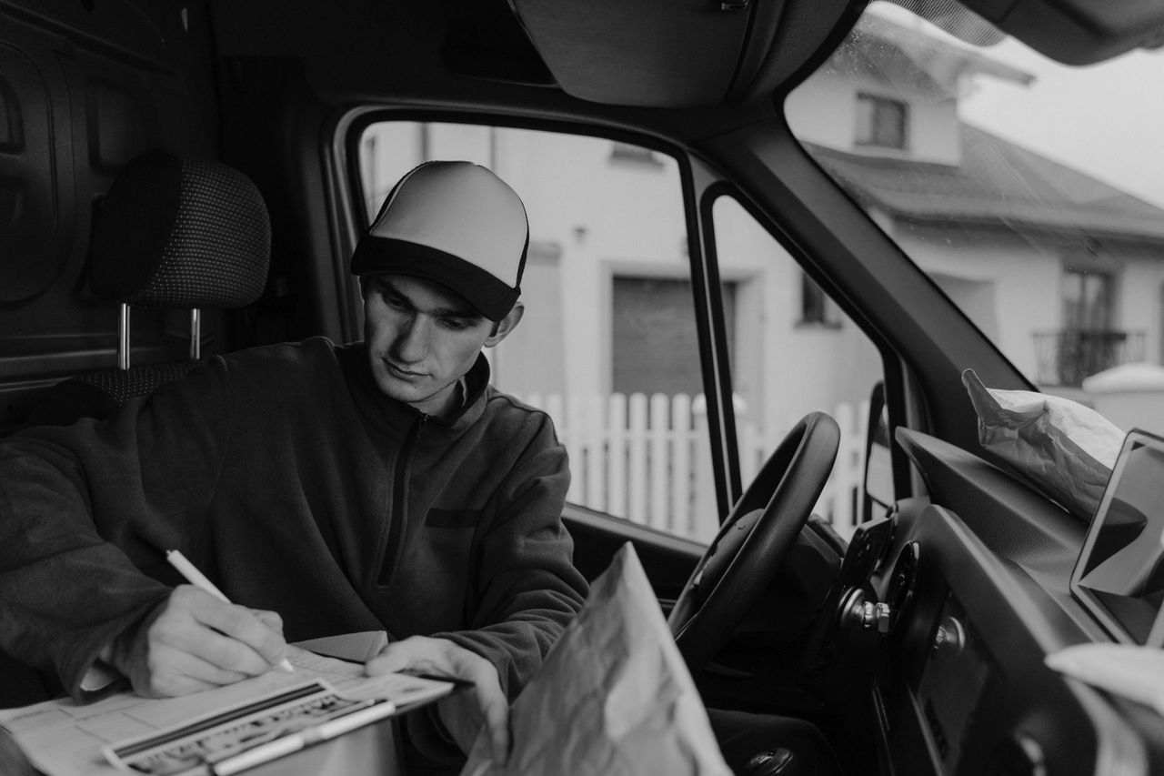about-us Black-and-white photo of a delivery driver organizing packages in a van.